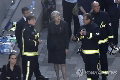 (런던 AFP=연합뉴스) 테리사 메이 영국 총리(왼쪽 3번째)가 15일(현지시간) 대형 화재가 발생한 런던 시내 고층아파트 '그렌펠 타워'를 방문, 소방당국의 설명을 듣고 있다. 메이 총리는 이날 화재 현장을 방문한 뒤 "이 끔찍한 비극이 제대로 조사되고 있다는 것을 확실히 하기 위해 진상조사위원회를 꾸리겠다"고 약속했다.       lkm@yna.co.kr