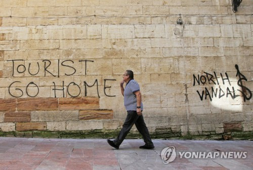 한 남성이 스페인 북부 도시 오비에도 시청 인근 벽에 써진 '관광객은 꺼져라'라는 문구 앞을 지나고 있다. [EPA=연합뉴스]