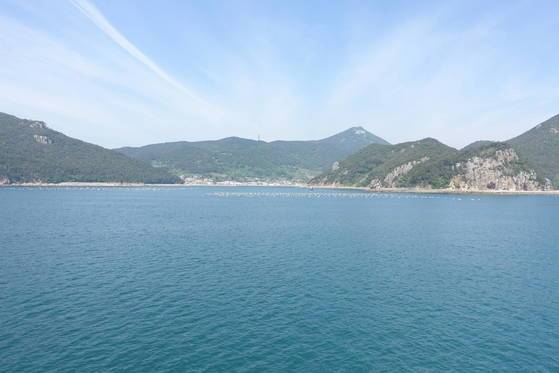 미륵도·한산도 사이 뱃길에서 본 태화물산의 3배체 ‘여름 굴’ 양식장. 바다 가운데 두 개의 바위가 떠 있는 것처럼 보인다. 가운데 작은 바위를 동네 사람들은 복바위 또는 아들바위라고 부른다. 그 앞에 떠있는 하얀 부표 아래서 굴들이 자라고 있다. 멀리 미륵산 정상이 보인다. 정상 아래 하얀 구조물은 여행객들이 많이 찾는 통영 케이블카 터미널이다.