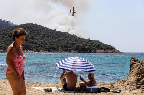 해변에서 보이는 산 위로 산불이 발행해 살수 비행기가 화마를 진압하고 있다. [AFP=연합뉴스]