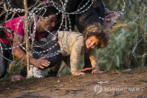 (로스케<헝가리> AP=연합뉴스) 27일(현지시간) 한 난민 어린이가 국경에 설치된 철조망 아래로 기어 세르비아에서 헝가리로 들어가고 있다.