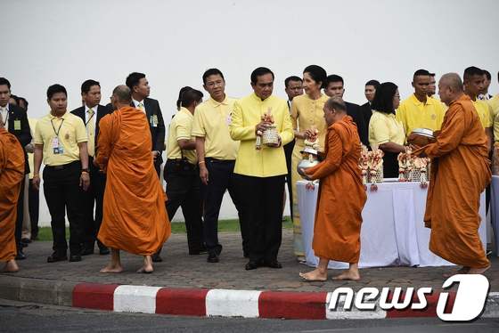 노란 의상을 입은 프라윳 찬호차 태국 총리(가운데)가 9일(현지시간) 방콕 왕궁 인근 지역에서 탁발 의식을 치르고 있다. © AFP=뉴스1