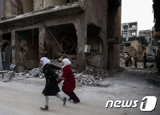 전쟁으로 폐허가 된 시리아 두마 건물 사이를 시리아 소녀들이 지나고 있다. © AFP=뉴스1