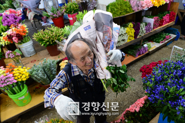 박창규씨가 꽃도매상가 매장에서 배달할 꽃을 넘겨 받아 어깨에 메고 있다./정지윤기자