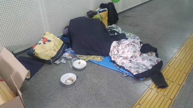 한 노숙인이 지하철 서울역사 안에 침낭을 깔고 그 안에 들어가 잠들어 있다.
