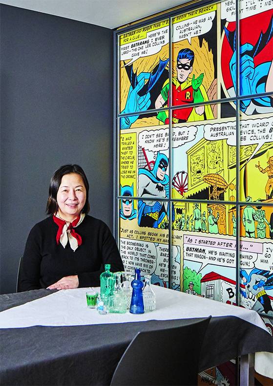 인테리어 디자이너 김정현 실장이 거실 중앙 식탁에 앉아 있다. 거실의 가장 넓은 벽을 진회색으로 칠하고, 다른 한쪽 벽에는 외국 사이트에서 구입한 총천연색 배트맨 만화 벽지를 발라 전체적으로 생기 넘치는 분위기를 연출했다. [양성모 프리랜서]