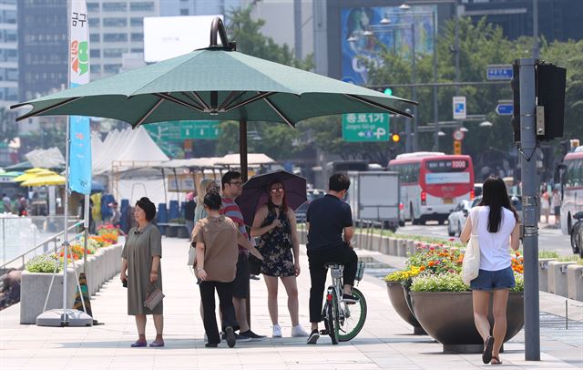 시민과 관광객들이 지난 1일 서울 광화문 광장에 설치된 그늘막 아래에서 보행 신호를 기다리고 있다. 연합뉴스
