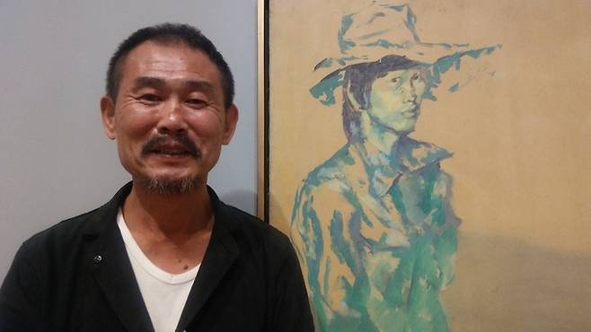 자신의 젊은 시절 자화상 앞에서 웃으며 이야기하는 최민화 작가. 이 그림은 ‘모자를 쓴 자화상’으로 홍익대 재학중인 1976년에 그린 것이다.