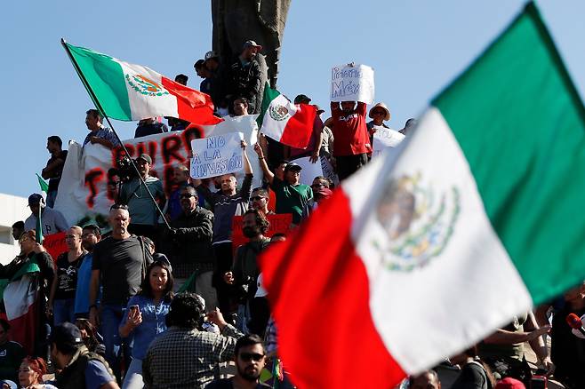 멕시코 시민들이 18일(현지시간) 티후아나 시에서 멕시코 국기를 흔들며 이민자 반대 시위를 벌이고 있다. [로이터=연합뉴스]