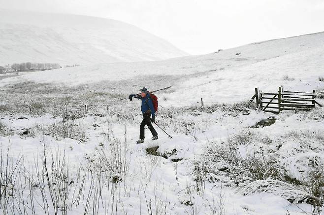 30일(현지시간) 밤새 눈이 내린 영국 웨일스의 브레콘비콘스국립공원에서 한 남성이 스키를 맨 채로 언덕을 가로질러 가고 있다.  웨일스｜AP연합뉴스