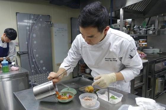 꿩김치를 상에 내기 위해 꿩고기와 토종 고수 어린잎, 식용 꽃잎 등 고명을 다 얹은 다음 마지막으로 김칫국물을 붓는 권우중 셰프.