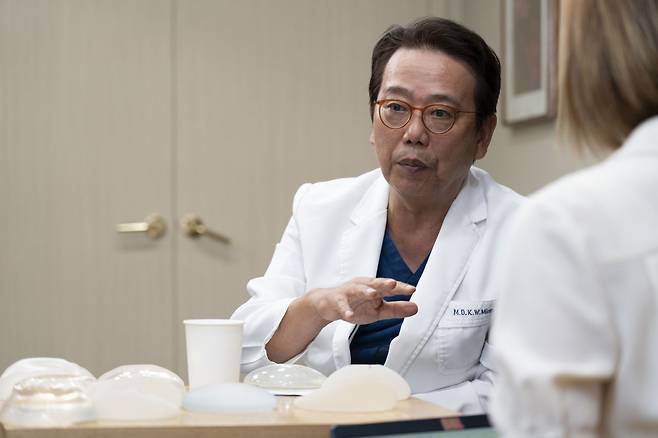 Minn Kyung-won, professor emeritus at Seoul National University Hospital, speaks to The Korea Herald. Types of breast implants are displayed on the table. (The Korea Herald)