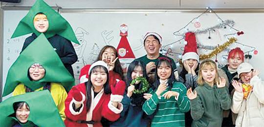 고도현 교사와 학생들이 크리스마스를 맞아 산타클로스와 트리 등의 복장을 하고 교실 칠판 앞에서 미소를 짓고 있다.