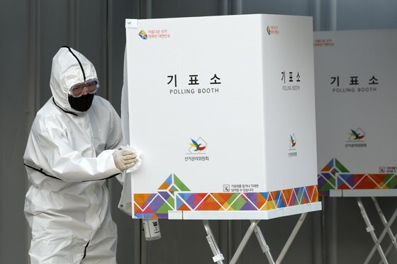 제21대 국회의원 선거일인 15일 오후 서울 종로구의 한 투표소에서 방호복을 입은 투표사무원이 자가격리자가 투표를 마치자 기표소를 소독하고 있다. 뉴스1