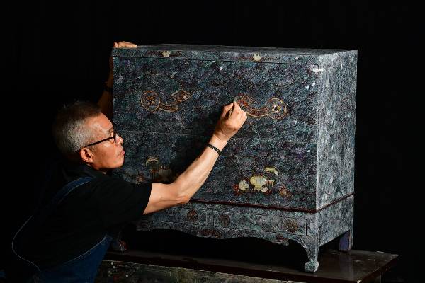 나전칠기 장인 유철현씨가 지난 10일 경기도 남양주 마석가구단지 청봉옻칠공방에서 현대적 감성으로 디자인한 반닫이의 마무리 작업을 하고 있다. 푸른빛과 회색빛이 감도는 자개를 잘게 쪼개 물보라가 이는 모습을 표현했다.