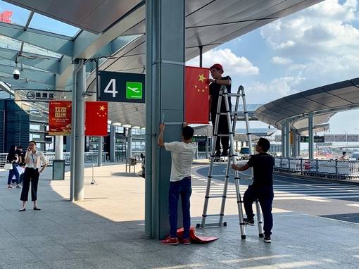 17일 중국 상하이 홍차오국제공항 2터미널 청사 바깥 기둥에 남성들이 중국 국기인 오성홍기를 걸고 있다. 오는 10월 1일 중국 건국 70주년 국경절을 기념해 ‘국가 경사를 즐겁게 보내자’는 의미로 환두궈칭(歡度國慶)이라 쓰인 깃발도 함께 걸려 있다. /상하이=김남희 특파원