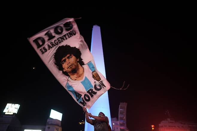 아르헨티나의 한 국민이 25일 부에노스아이레스 인근의 한 빈민가에서 마라도나의 얼굴이 그려진 깃발을 흔들며 마라도나의 죽음을 애도하고 있다. 부에노스아이레스 | AP연합뉴스