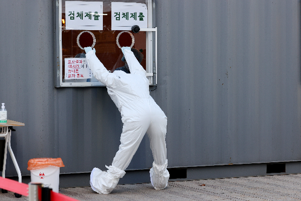 국내 신규 확진자 수가 1200명대를 기록한 25일 오후 업무에 지친 의료진 한 명이 서울 중구 서울광장에 마련된 임시선별진료소에서 검체 제출구를 붙잡고 몸을 풀고 있다. 연합뉴스