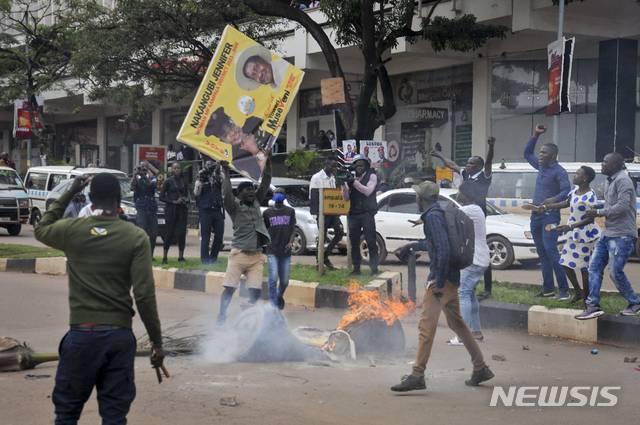 [캄팔라=AP/뉴시스]18일(현지시간) 우간다 수도 캄팔라에서 야당 대통령 후보 보비 와인(본명 로버트 캬굴라니)을 지지하는 시위대가 요웨리 무세베니 현 대통령의 사진이 담긴 현수막을 불에 태우려 하고 있다. 우간다 경찰은 내년 대선에서 대통령을 노리는 음악가 겸 야당 지도자 보비 와인이 경찰에 체포된  후 시위가 벌어져 3명이 숨지고 38명이 다쳤다고 밝혔다. 2020.11.19.