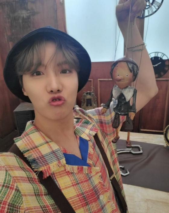 Another photo featured J-Hope sitting in a white suit in the atmosphere, taking a mirror selfie, and J-Hope posing as if he were taking a picture with his face on Camera.