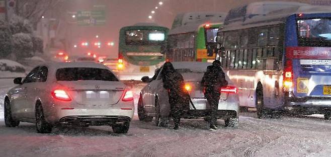 퇴근길 폭설에 교통대란… 서울 오늘 체감온도 영하 23도 - 6일 밤 눈으로 뒤덮인 서울 강남구 삼성역 인근 도로에서 시민들이 월동 장구를 갖추지 못한 차량을 밀어 이동시키고 있다. 이날 오후 9시 기준 서울에 3.8㎝, 경기 과천에 10.8㎝ 눈이 쌓이는 등 폭설이 내려 수도권, 강원 영서, 충청, 전라, 제주 산지에 대설주의보가 발효됐다. 기상청은 7일에도 서울 최저기온이 영하 14도까지 떨어지는 등 추위가 이어질 것이라고 예보했다. /연합뉴스