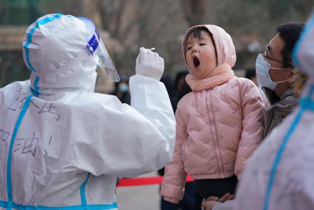 코로나19 감염 확산으로 도시가 봉쇄된 중국 베이징 인근 허베이성 스자좡에서 6일 방호복을 입은 방역요원이 어린 아이의 입에서 검체를 채취하고 있다. 스자좡=AP 연합뉴스