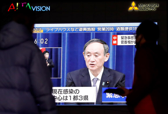 일본에서 코로나19 감염자가 걷잡을 수 없이 증가하고 있는 가운데 7일 스가 요시히데 총리가 앞으로 한 달 동안 도쿄도 등 수도권에 긴급사태를 선포한다고 밝히는 모습을 행인들이 TV를 통해 지켜보고 있다.도쿄 로이터 연합뉴스