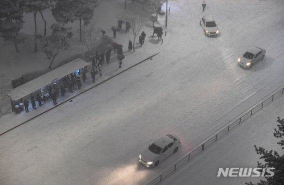 지난 6일 밤 경기도 수원시 영통구 망포동에서 퇴근길 시민들이 눈이 도로를 완전히 뒤덮은 도로 사이에서 버스를 기다리고 있다.