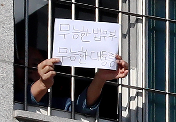 지난 6일 서울 송파구 동부구치소에서 한 수용자가 '무능한 법무부 무능한 대통령'이라고 쓴 종이를 창문 밖 취재진에게 내보이고 있다./연합뉴스