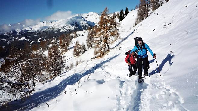 눈길을 힘들게 오르는 도미니크 뒤로 오스트리아의 산군이 펼쳐진다.