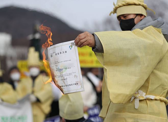 한국유흥음식업중앙회 경남도지회원이 21일 오후 경남 창원시 의창구 경남도청 입구에서 영업 허가증을 불에 태우고 있다.  이 단체는 코로나19 관련 사회적 거리두기 방역 완화 대상에서 제외된 것에 반발해 이날 기자회견을 열고 허가증을 불에 태웠다. /연합뉴스