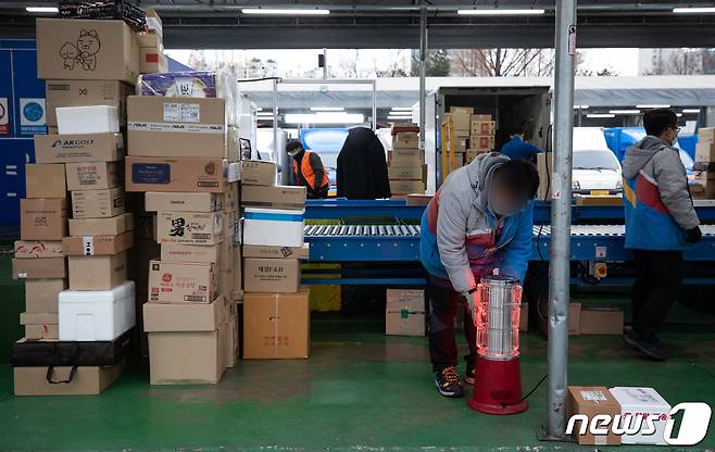 28일 서울시내 한 택배 물류센터에서 한 택배 노동자가 분류 작업 중 언 손을 녹이고 있다. 2021.1.28/뉴스1 © News1 유승관 기자