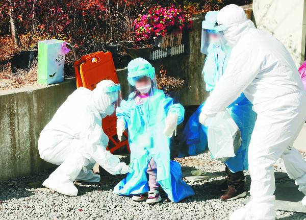 방역당국 관계자들이 27일 광주 광산구 운남동 TCS국제학교 앞에서 이 학교에 머물던 어린이에게 방역복을 입히고 있다. 이 학교에선 합숙생활을 하던 재학생 등 113명이 코로나19에 감염됐다. 연합뉴스