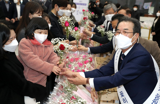 Nonghyup Chairman Lee Sung-hee, right, hands flowers to a child at the banking group's headquarters in Jung District, central Seoul on Monday. As part of efforts to help hard-hit flower farmers amid the coronavirus pandemic, Nonghyup gave away 1,000 vases filled with 2,500 flowers to employees. [YONHAP]