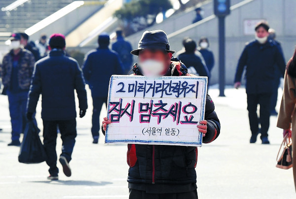 한 노숙인이 31일 서울역 앞 광장에서 ‘2미터 거리 간격 유지 잠시 멈추세요’라고 적힌 손팻말을 들고 있다. 정부는 이날 현행 사회적 거리두기 단계를 2주 더 연장했다. 권현구 기자