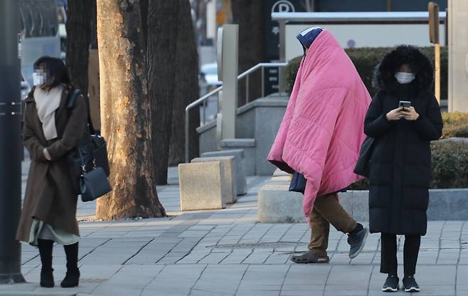 반짝 추위가 찾아온 8일 오전 서울 시내에서 한 시민이 이불을 쓰고 지나가고 있다. [연합]