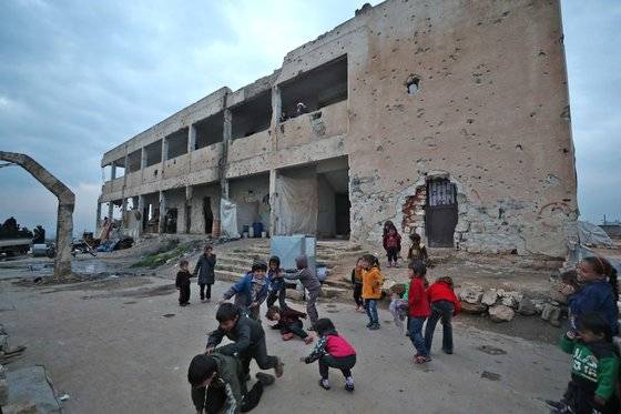 터키 국경과 가까운 시리아 서북부 이들립의 국내 피란민 킴프에서 지난 3월 2일 어린이들이 놀고 있다. 뒤에 보이는 것이 전투로 심하게 훼손된 학교 건물이다. 아직 어린이들에 대한 교육은 시작하지 못하고 있다. AFP=연합뉴스