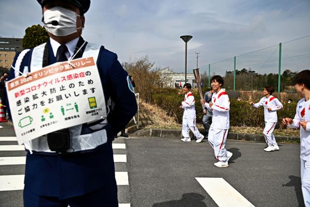 지난달 25일 일본 후쿠시마현 나라하에서 진행된 도쿄올림픽 성화 봉송 행사에서 한 경찰관이 코로나19 예방 협조 표지판을 목에 걸고 있다. 나라하=로이터 연합뉴스