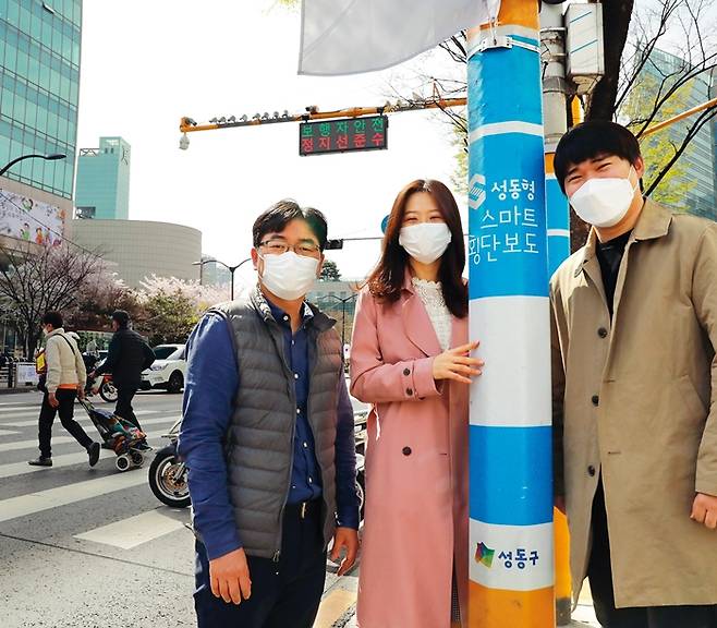 성동구가 ‘스마트 포용도시’ 비전 실현을 위해 적정기술을 활용한 생활 불편 해결에 나서는 가운데 공무원 동아리 ‘성동적정기술연구회’는 3년째 활동을 이어오며 적정기술 활용 마인드를 높여왔다. 사진은 1일 성동구청 앞 스마트횡단보도 안내문 앞에 선 성동적정기술연구회의 (왼쪽부터) 민상현·남혜진 팀장, 유경민 주무관의 모습.
