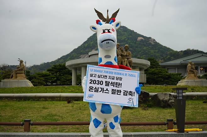 Kirini the blue-spotted giraffe holds up a sign in front of the presidential office in central Seoul. It reads, “2030 coal phaseout! Cut greenhouse gas emissions in half!” (Korea Beyond Coal)