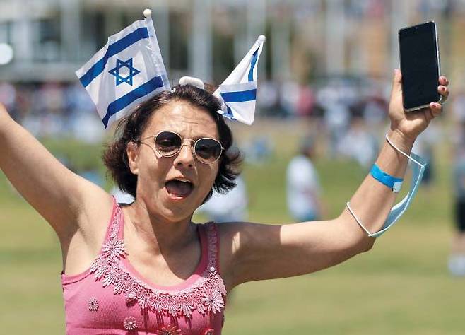 접종률 세계 1위 이스라엘, 야외 노마스크 허용 - 이스라엘 독립기념일인 15일(현지 시각) 수도 예루살렘의 공원을 찾은 여성이 국기를 머리에 꽂은 채 즐거워하고 있다. 세계에서 코로나 백신 접종 속도가 가장 빠른 이스라엘은 18일부터 실외 마스크 착용 의무를 폐지하기로 했다. /로이터 연합뉴스