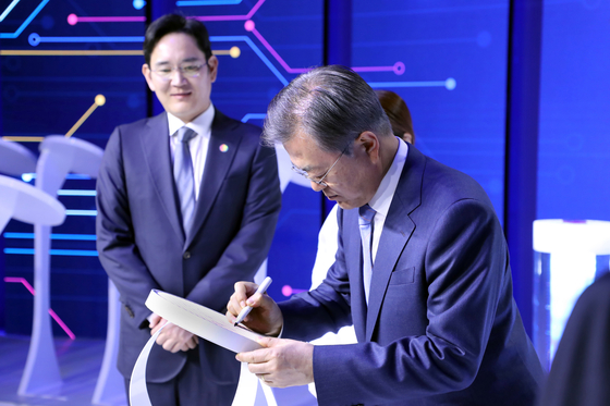 Flanked by Samsung Electronics’ Vice Chairman Lee Jae-yong, left, in its Hwaseong plant on April 2019, President Moon Jae-in signs on the world’s first 7-nanometer circuit wafer the company developed using extreme ultraviolet (EUV) lithography equipment on the sidelines of the government declaration of the “System Semiconductor Vision.” [YONHAP]