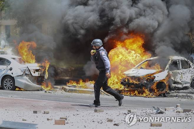 이스라엘 남부 애슈켈론에서 지난 11일 승용차가 가자지구에서 날아온 로켓에 맞아 불타는 가운데 이스라엘 소방관이 지나가고 있다. [AP=연합뉴스 자료사진]