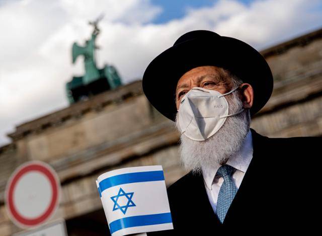 20일 독일 베를린 브란덴부르크문 앞에서 열린 반유대주의 반대 집회에 참석한 한 랍비가 이스라엘 국기를 들고 서 있다. 베를린=EPA 연합뉴스