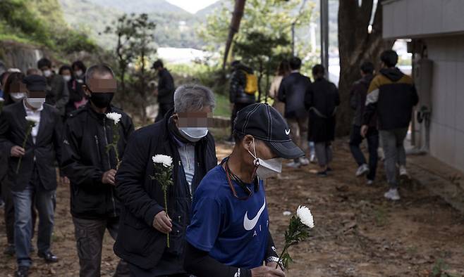 지난해 10월 14일 경기 파주시 '추모의 집'에서 추모객들이 마스크를 쓴 채 국회를 들고 입장하고 있다. 1년에 단 한 번 열리는 이날 합동 위령제에선 쪽방촌 주민 등 고인의 생전 이웃과 친지들이 참석해 헌화했다. 나눔과 나눔 제공