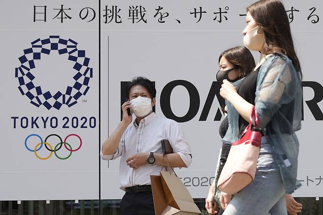 일본 수도 도쿄에서 25일 신종 코로나 바이러스 감염증(코로나19) 예방 마스크를 쓴 시민들이 개막이 채 한 달도 남지 않은 도쿄올림픽의 포스터 앞을 지나고 있다. 일본은 최근 코로나 신규 확진자 수가 연일 1천700명대를 기록해 올림픽을 코앞에 두고 재차 증가 조짐을 보이고 있다. /연합뉴스