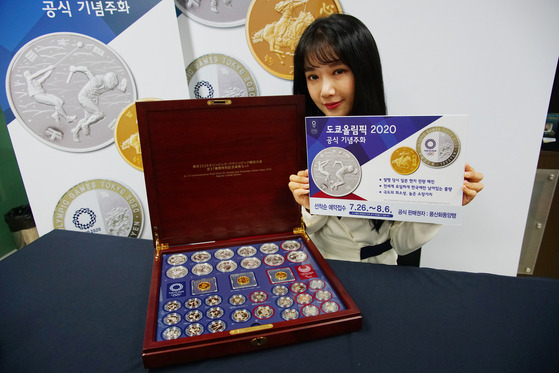 A model holds up coins commemorating the 2020 Tokyo Olympics, which officially starts on Friday. The coins are sold by Poongsan Hwadong. The Tokyo Olympics was postponed by a year due to the Covid-19 pandemic, the first Games ever to be delayed. Poongsan Hwadong has been selling the commemorative coins since the 1952 Helsinki Games. [POONGSAN HWADONG]