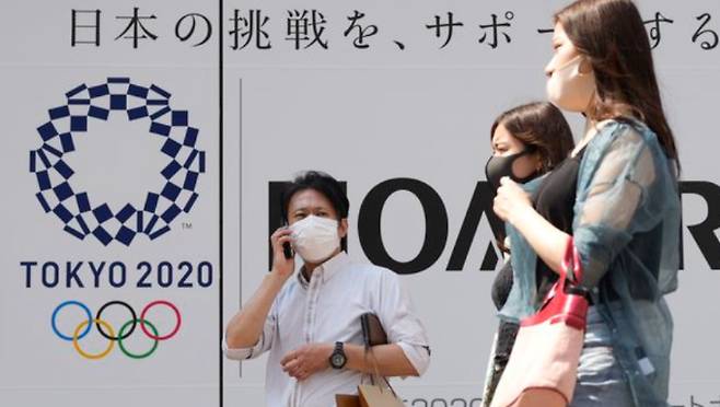 일본 수도 도쿄에서 25일 신종 코로나바이러스 감염증(코로나19) 예방 마스크를 쓴 시민들이 개막이 채 한 달도 남지 않은 도쿄올림픽의 포스터 앞을 지나고 있다. 연합뉴스 제공