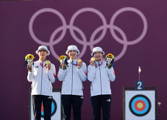 From left to right, An San, Jang Min-hee and Kang Chae-young of the Korean women’s archery team hold up their gold medals after winning the final match against Russia in three straight sets on Sunday at Yumenoshima Park Archery Field in Tokyo. [JOINT PRESS CORPS]