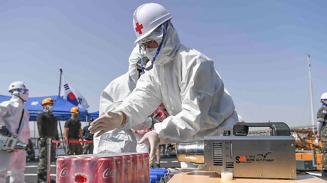 지난 3월 모항인 오만 무스카트항에서 크레인을 이용해 선적한 물품을 소독하는 청해부대원들. 방호복과 장갑, 마스크를 착용하고 있다.